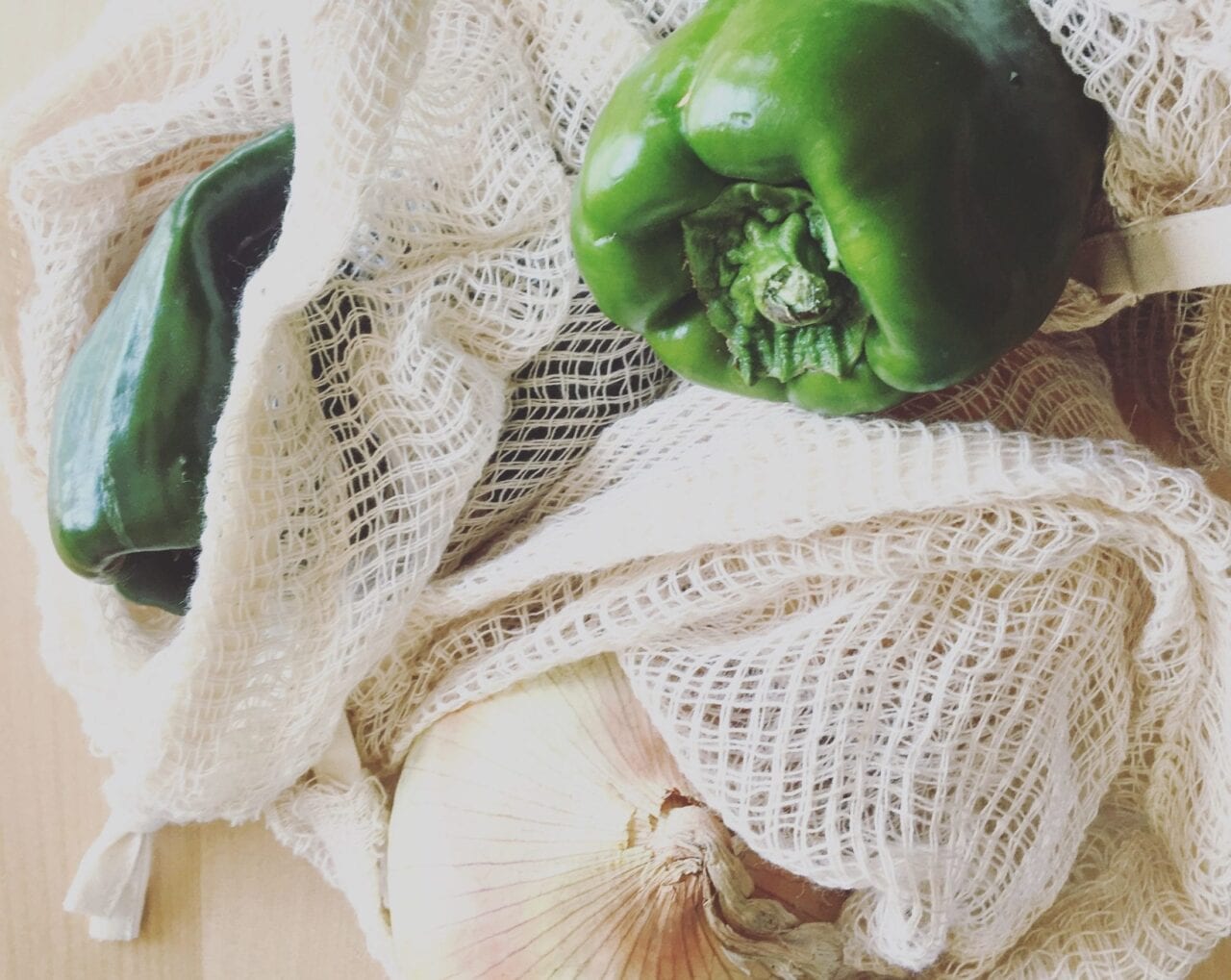 Vegetables in mesh fabric bags sit on a wooden table.