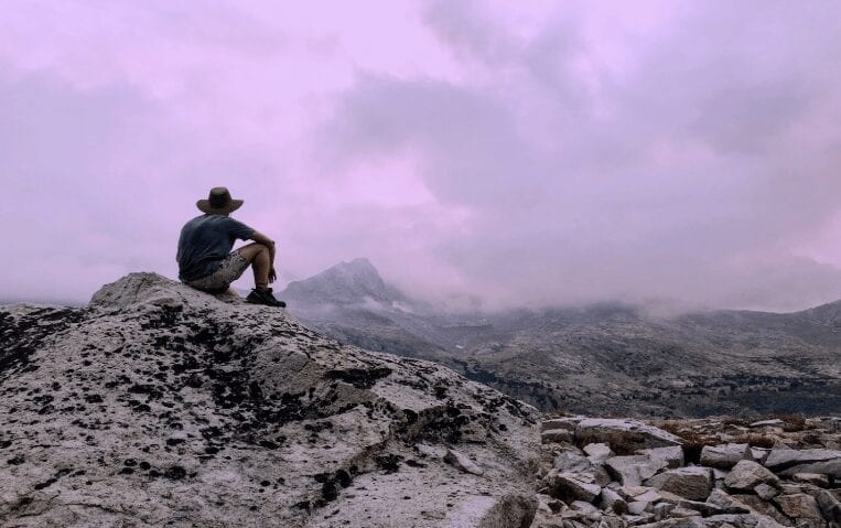 A hiker sitting on a mountain with a cloudy purple sky.