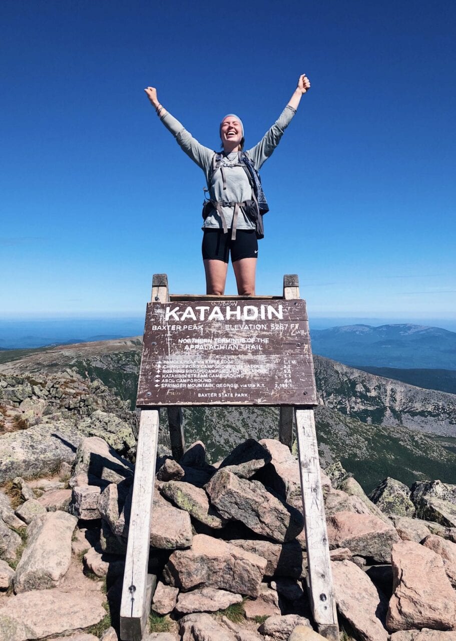 A hiker standing on top of the Mount Katahdin sign on the Appalachian Trail.