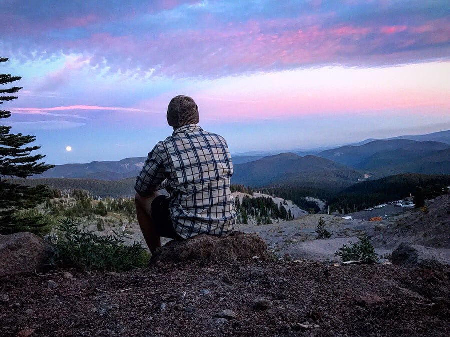 A hiker sitting and looking out at the sunset.