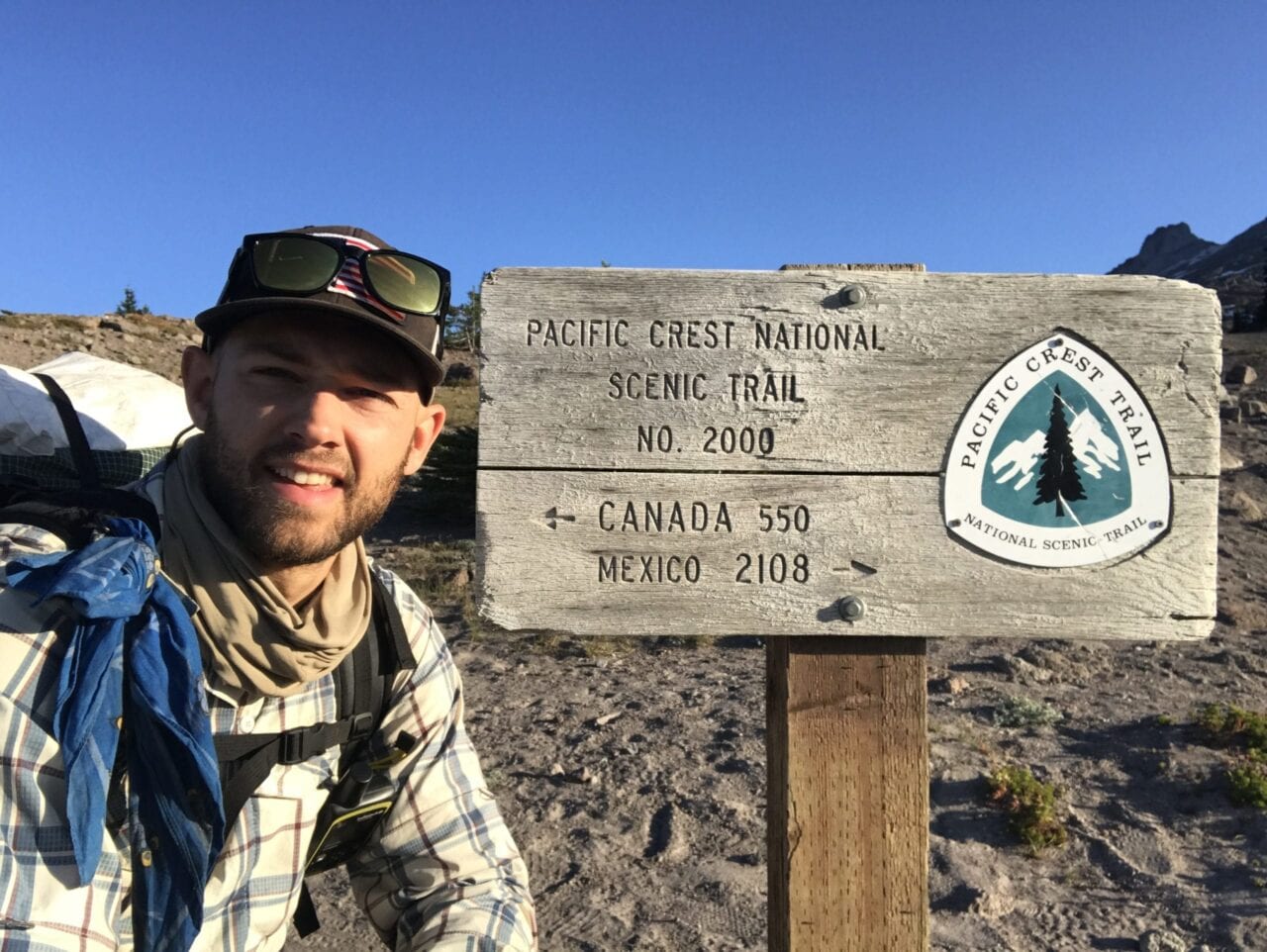 A hiker posing next to a Pacific Crest Trail sign.