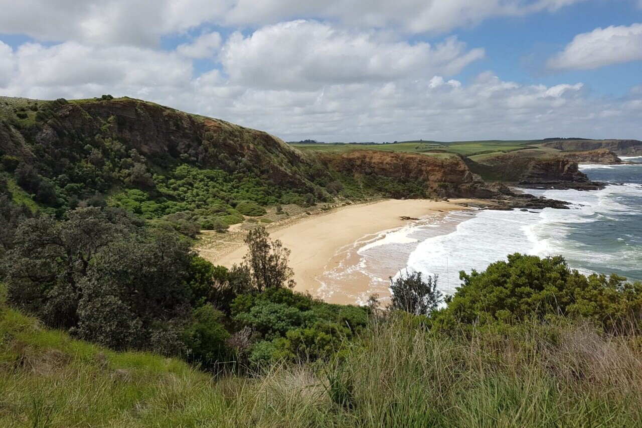 Ocean waves lap a wide sandy beach below green headlands.