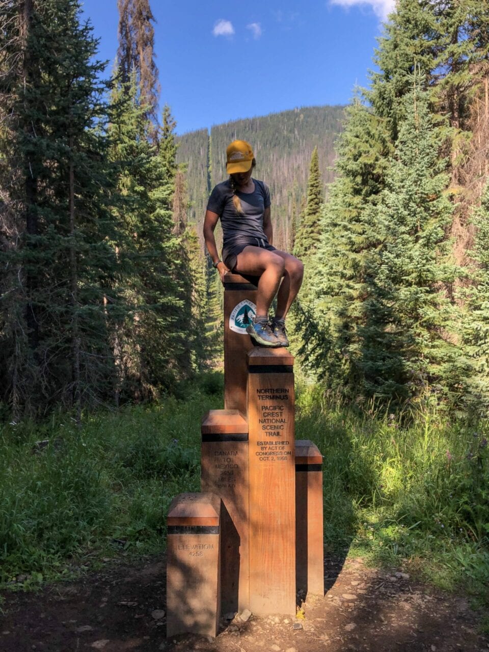 A woman sitting on top of the PCT Northern Terminus.