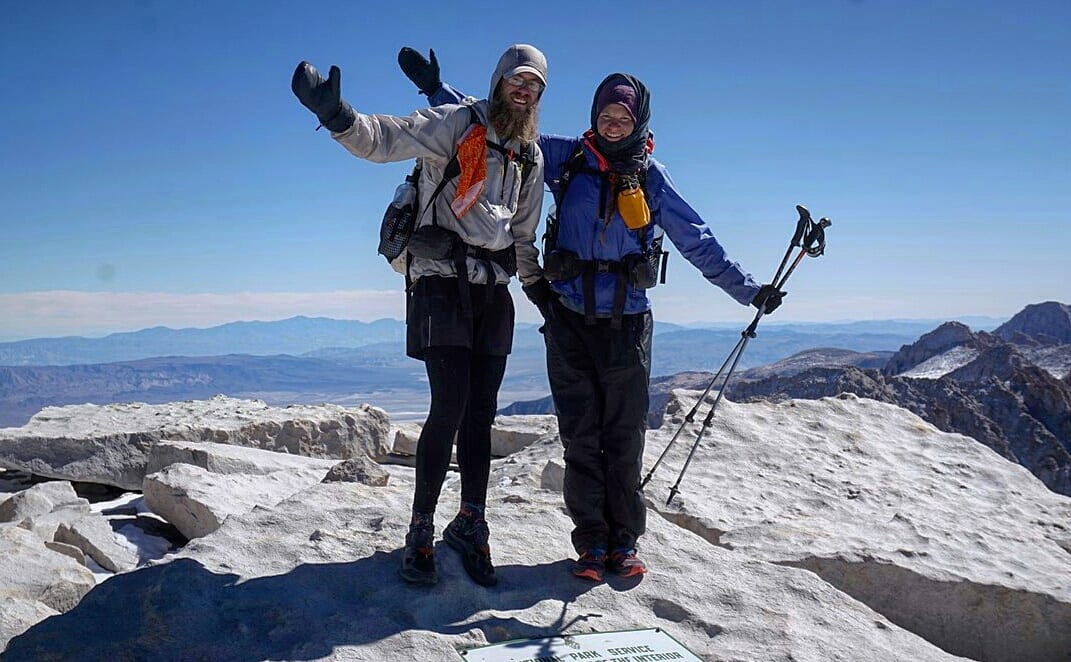 Two hikers standing on top of a mountain with their arms up.