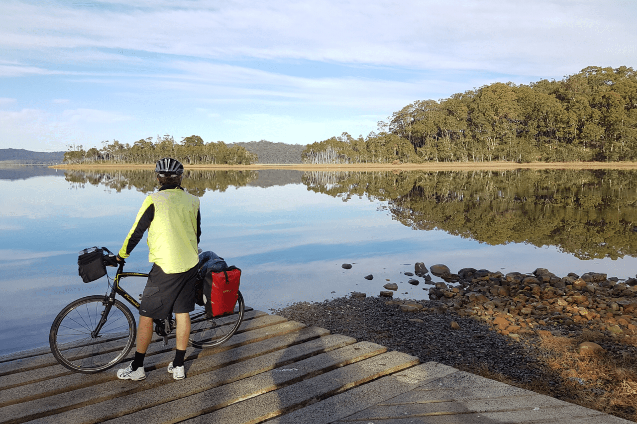 A person standing next to their bike looking out at water.