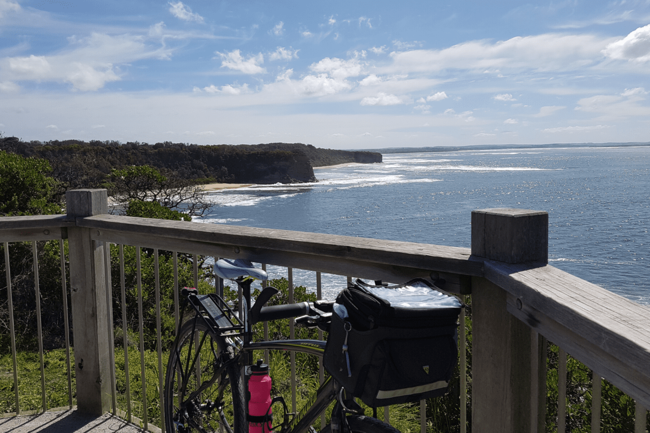 A bike propped up again a fence with a view of the ocean.