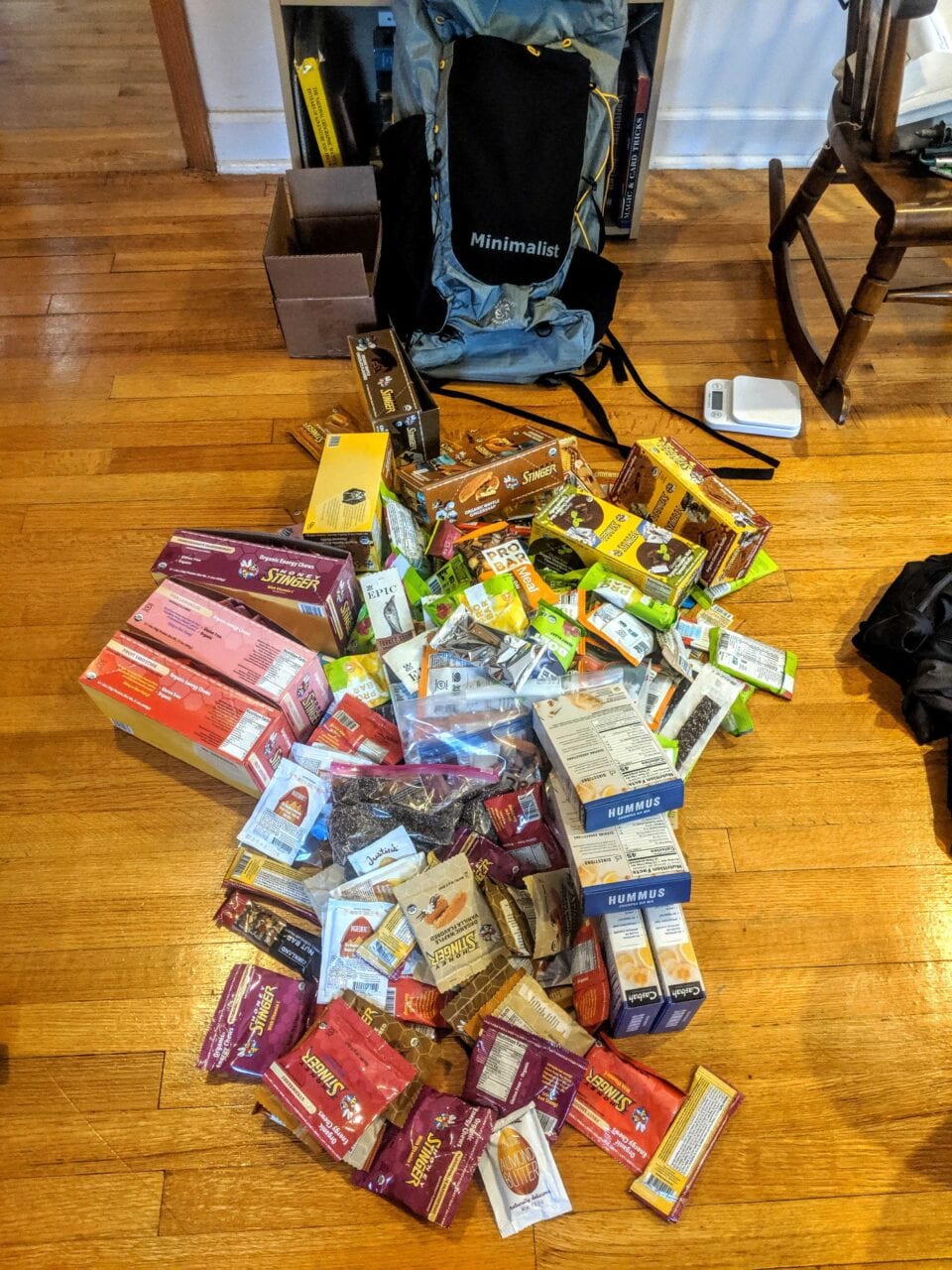A pile of backpacking food on the ground in front of a backpack.