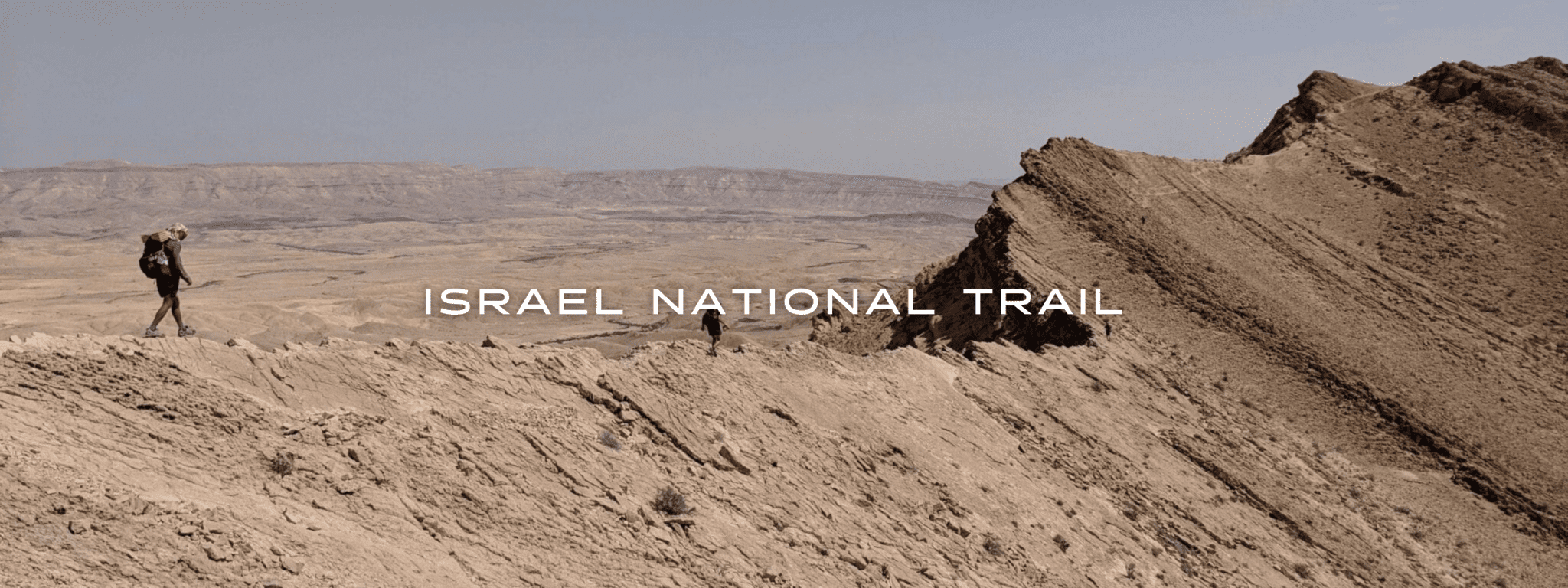 Two hikers walk along the knife's edge of a jagged cliff in teh desert.