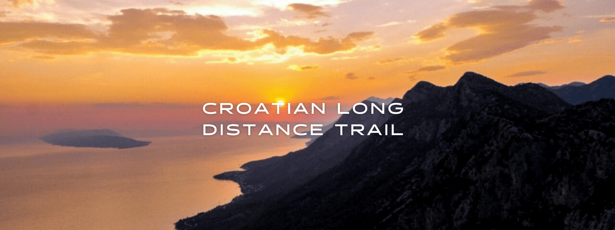 The sun sets over a mountain range and a large body of water on the Croatian Long Distance Trail.