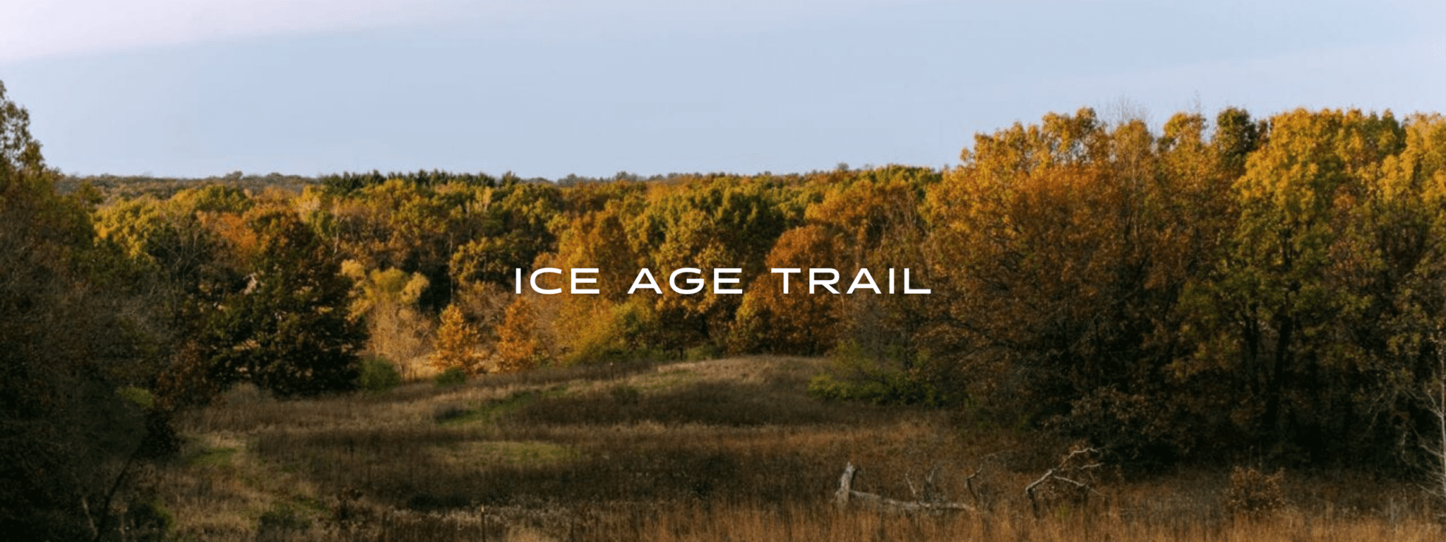The Ice Age Trail winds through a meadow towards a deciduous forest of Autumn colors.