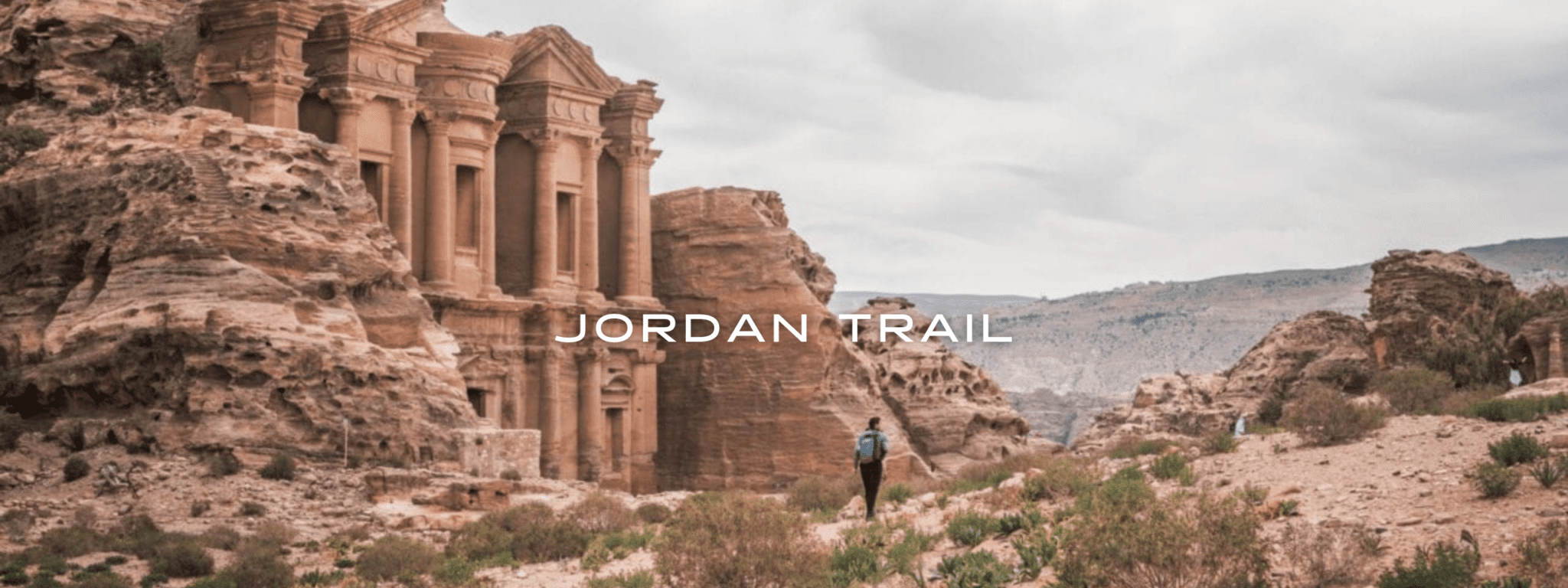 A hiker walks through a desert landscape near a historic structure.