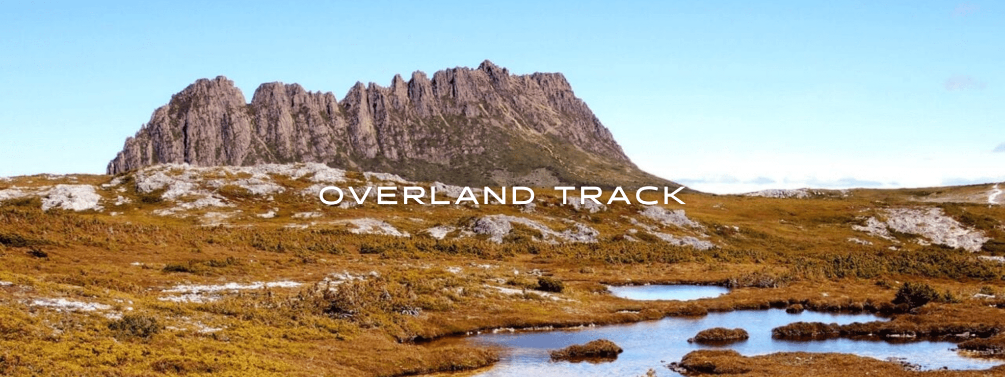 A solitary rocky mountain juts through a red grassy landscape.
