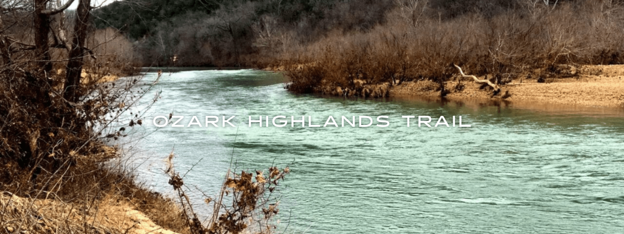 A blue river flows through a deciduous forest and sandy shores.