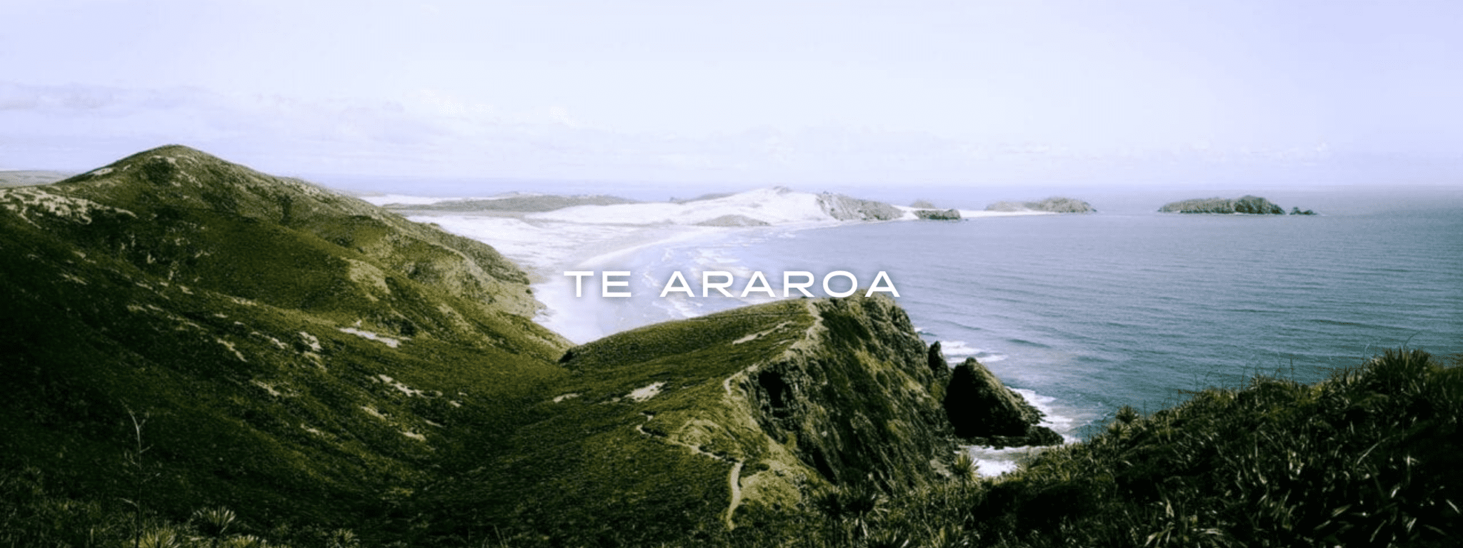A view from Cape Reinga on the Te Araroa on the North Island of New Zealand looks over beautiful blue ocean, white sand beaches, and green hills.