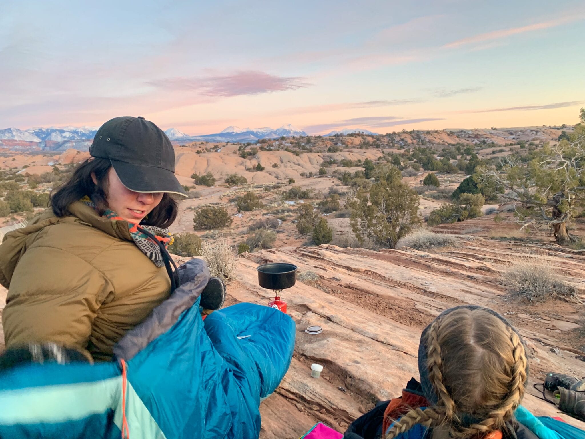 Two hikers make dinner on a stove at sunset