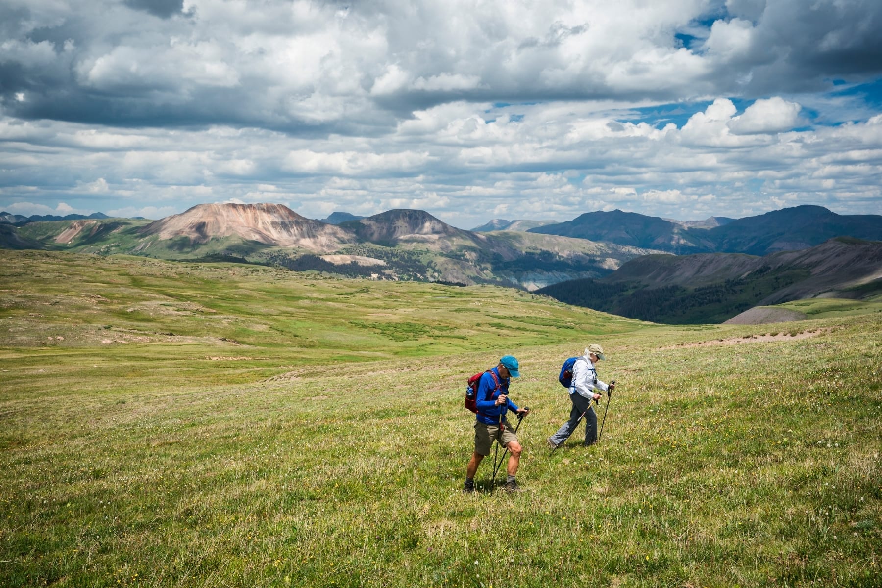 A man and woman hiking on a big grassy field