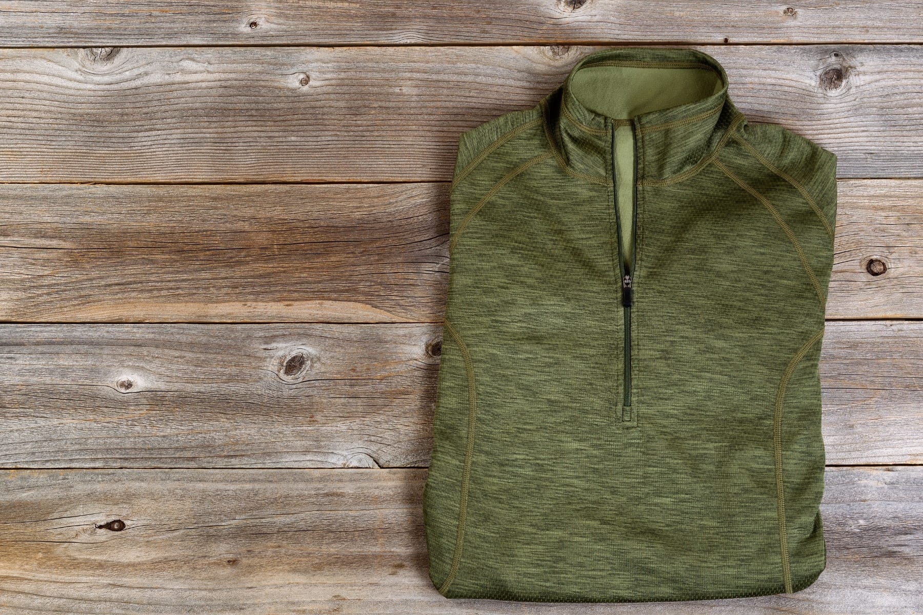 A green zip up jacket folded on a wooden background.
