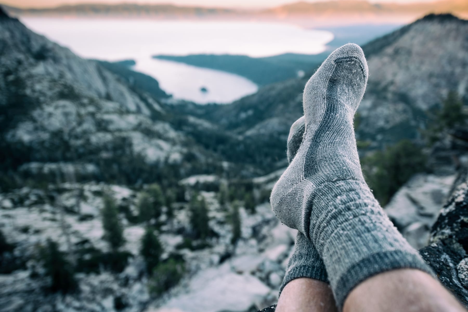 A person wearing socks with a view of mountains and a lake in the background.
